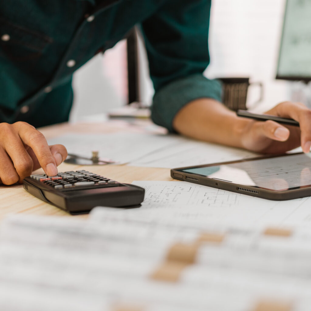 close up architect or engineer pressing on calculator for calculating value estimating for safety with the drawing construction building.